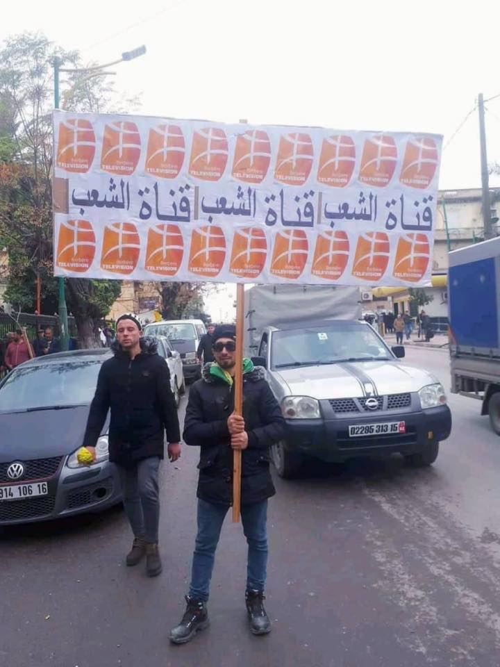 Pancarte portée par un manifestant du Hirak algérien, ou la Révolution du Sourire, sur laquelle on peut lire en arabe : « BRTV, la chaîne du peuple » (photo prise le vendredi 10 janvier 2020 et reprise par la chaîne sur ses réseaux sociaux, ©D.R.).